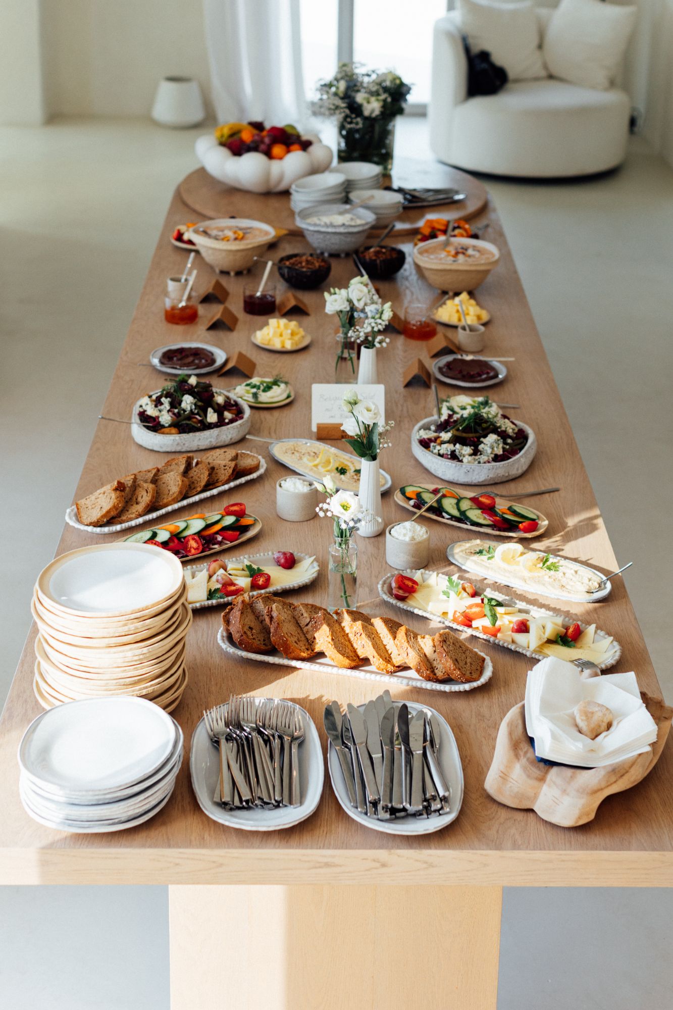Lange Holztafel mit Brot, Salaten, Dips und Blumen